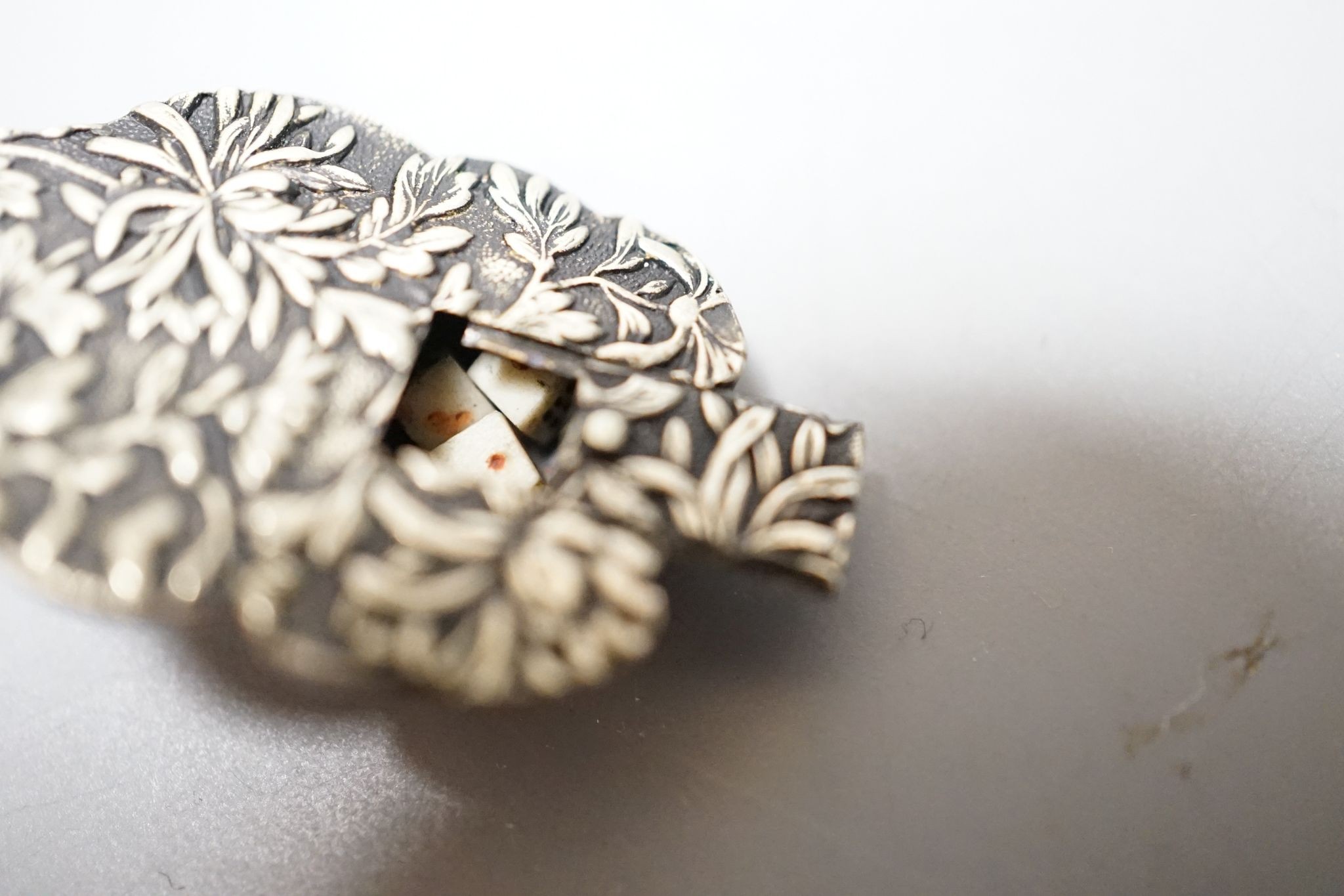 An unusual Japanese mixed metal noh mask containing minute bone dice and a stag antler noh mask brooch, signed, 3.5cm